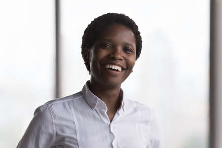 Happy confident millennial African businesswoman in formal shirt head shot portrait. Successful CEO, executive, female business leader, company owner looking at camera with toothy smile in officeの写真素材