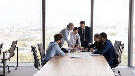 Team of interns and teacher studying marketing, working on startup project together. Business coworkers brainstorming, negotiating on sales reports at table in meeting room. Teamwork conceptの写真素材