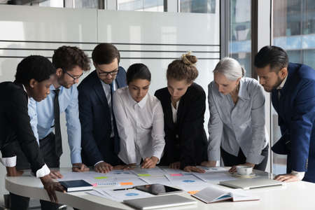 Multiethnic business team meeting over project marketing reports, analyzing paper charts with sticky notes, using scrum method, working on strategy, business plan. Diversity, teamwork conceptの写真素材