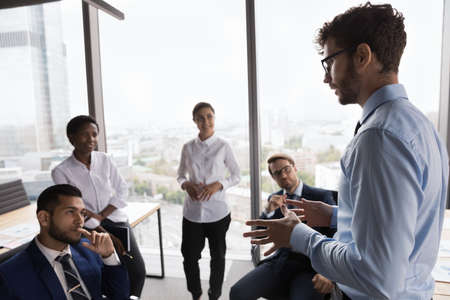 Serious young coach training diverse young business team. Charismatic company leader speaking before...