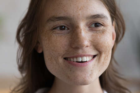 Happy freckled face of young pretty woman lost in positive thoughts looking away with toothy smile, thinking, dreaming. Cheerful girl with natural makeup close up facial portrait. Skincare conceptの写真素材