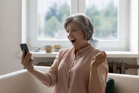 Happy surprised senior smartphone user woman looking at mobile phone, reading text message on gadget...