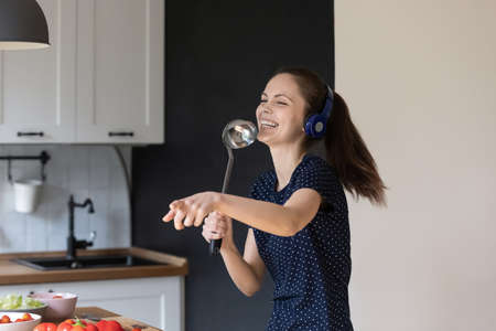 Excited joyful young girl enjoying domestic entertainment, singing songs at utensil object,...