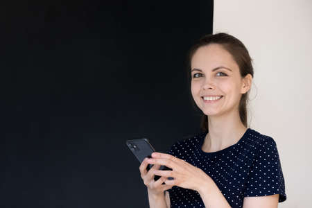 Happy cheerful smartphone user girl headshot studio portrait. Positive young woman holding mobile phone, using online app, chatting on Internet, looking at camera. Communication conceptの写真素材