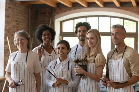 Group of happy diverse students led by professional aged teacher pose together in art studio workshop, smiling looking aside, feel inspired and motivated. Higher art education, creative hobby conceptの写真素材