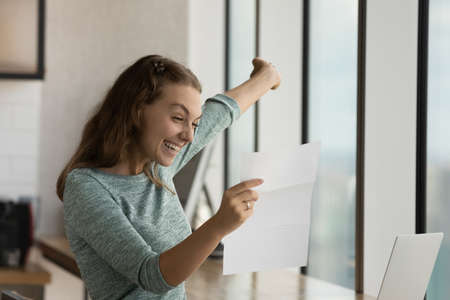 Happy excited student girl reading paper letter with good news, receiving admission letter from university, college, school, smiling, laughing, shouting for joy, celebrating achieve, successの写真素材