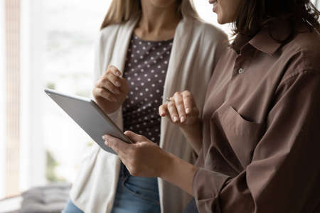 Female business coworkers using tablet together, watching virtual online presentation, discussing and reviewing project design. Businesswoman showing content on gadget screen to colleague. Close upの写真素材
