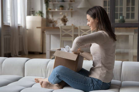 Happy curious impatient shopper opening carton box with purchase from internet shop, unwrapping package, holding paper container. Woman receiving parcel from order delivery serviceの写真素材