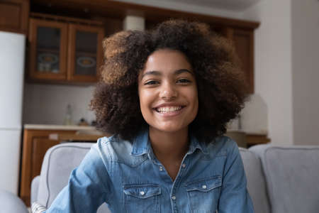Cheerful young Black woman video blogger sitting on couch streaming live looking at web camera...