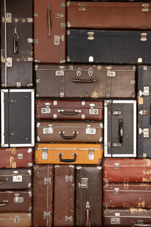 Wall of vintage antique stylish luggage cases. Old fashioned travel bags background. Texture from retro shabby leather stacked suitcases. Airport, journey, trip, adventure concept. Vertical shotの写真素材