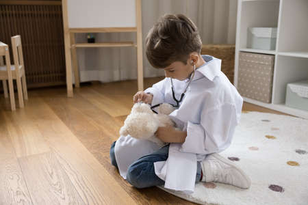 Little boy in uniform use stethoscope listens heartbeat to stuffed bear, takes care best toy friend, play doctor in imaginary clinic. Health-care, paediatrics, future profession and vocation conceptの写真素材