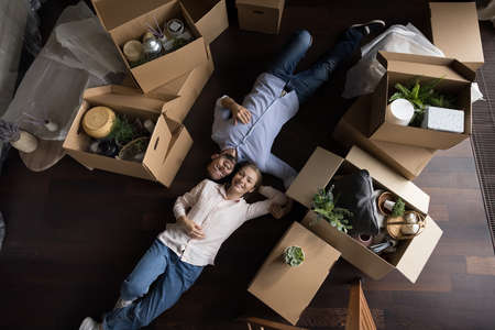 Top view happy married millennial couple relax on relocation day, ready to move out, lying on floor near stuff, personal belongings packed in big stacked cardboard boxes. New home, bank loan conceptの写真素材