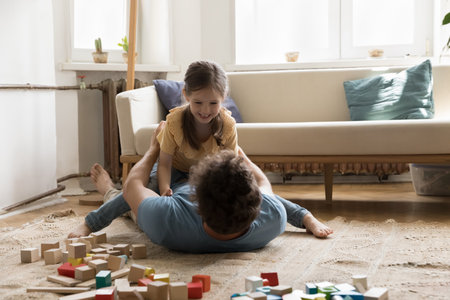 Playful sweet daughter kid resting dads chest, laughing, playing fighting game. Father lying on back on warm carpeted floor cuddling, caressing sweet child, enjoying fatherhood, playtime, leisureの写真素材