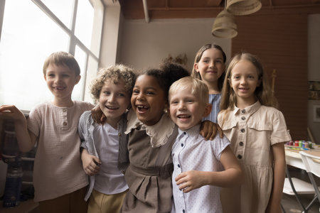 Group of cheerful diverse kids having fun in creative artistic space, hugging, laughing, smiling, looking at camera. Art school pupils, friends, classmates enjoying leisure in classroomの写真素材