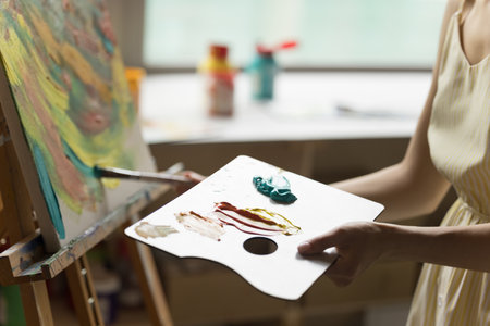 Artist using craft palette for drawing picture, holding pad with colorful acrylic paints, stroking...