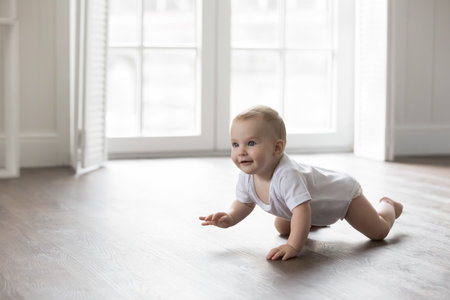Happy baby in bodysuit crawling on knees on clean warm floor. Cheerful active little infant kid training physical skills, looking away, smiling. Pretty adorable infant kid home portraitの写真素材