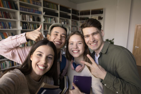 Multiethnic best friends, girls and guys, students standing in library looking at smartphone screen make selfie picture, gesturing, record vlog for channel. Generation Z, modern tech, studentship, funの写真素材