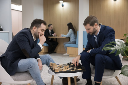 Two male business colleagues playing chess on work break, sitting at chessboard in office kitchen,...