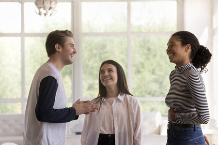 Three best friends, two girls and guy standing indoors, lead pleasant conversation meet in restaurant, public modern lounge place for hanging out of young people. Friendship, communication, pastimeの写真素材
