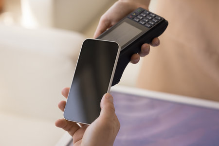 Unknown male client holds modern wireless gadget makes contactless payments by mobile phone, spend...