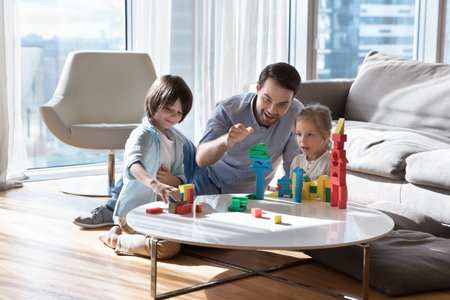 Excited cheerful dad enjoying leisure playtime with two little children, stacking toy tower with kids, teaching son and daughter to construct castle, enjoying parenthood, weekendの写真素材