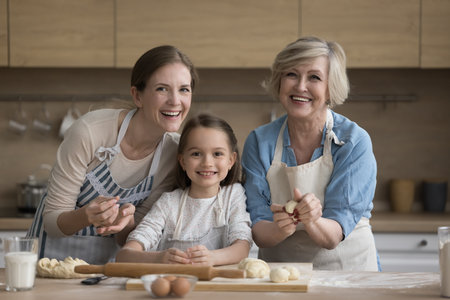 Portrait of multi generational women, cute little girl her older pensioner granny and young mother wear aprons cooking together homemade pastries, smile pose look at camera. Family pastime and cuisineの写真素材