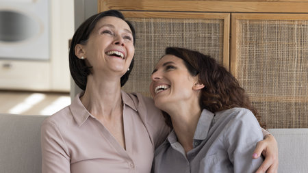 Cheerful mature mom and happy adult daughter woman excited with funny conversation, hugging, laughing, meeting at home, sitting close on couch, talking, smiling, laughing out loud. Banner shotの写真素材