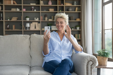 Happy mature senior woman showing greeting hello hand at smartphone, saying hi, talking on video...