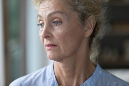 Bored sad lonely pretty senior woman looking at window away, thinking over problem, trouble, suffering from mental disorder, Alzheimer disease. Upset mature lady close up portraitの写真素材