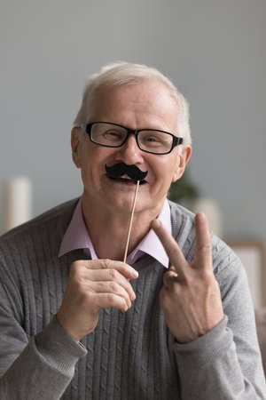 Vertical portrait carefree senior man having fun hold party accessory, celebrate life event or anniversary look at cam, advertises lenses and eyewear store, professional check up services of eyesightの写真素材