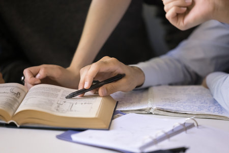 Close up of open scientific textbook and hands of students pointing at page. Group of classmates reading, discussing book together, meeting at table for studying in team, getting knowledgesの写真素材