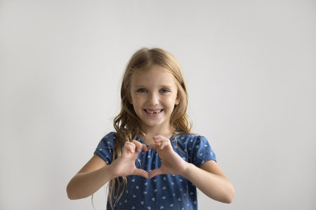 Cheerful cute preschool girl joining fingers, making hand heart shape, Positive pretty little kid showing gesture sign of happiness, love, care, support, enjoying happy childhood.の写真素材