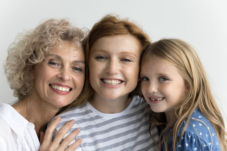 Cheerful cute little kid girl, pretty mom and grandma standing close, hugging with head touches,...
