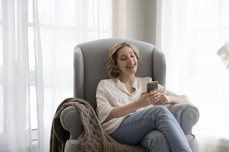 Happy young smartphone user woman enjoying online communication at home, resting in comfortable...