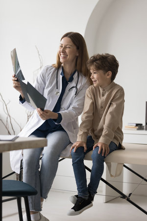 Cheerful practitioner reviewing Xray scan, shot of bones of little patient boy, feeling happy, smiling, laughing. Kid meeting with pediatrician doctor after radiography screening examinationの写真素材