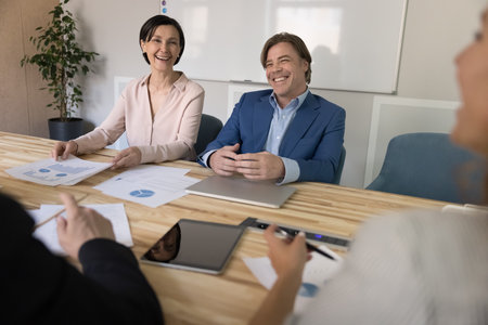 Cheerful mature couple of business colleagues discussing marketing strategy on office meeting,...