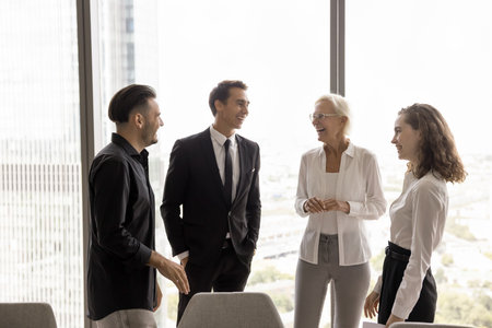 Happy younger and older business colleagues in formal clothes standing together at large office...
