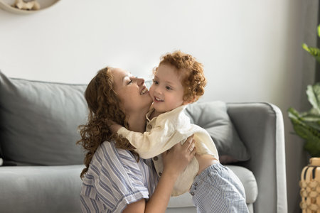 Happy caring young mom hugging cute red haired toddler son at home, playing with child on floor, cuddling, kissing cheerful kid, expressing love, affection, care, enjoying family mothers leisureの写真素材