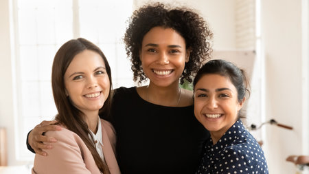 Close up portrait of smiling multiracial female employees colleagues posing in office together, happy young multiethnic diverse woman interns friends hug embrace show unity and support at workの写真素材