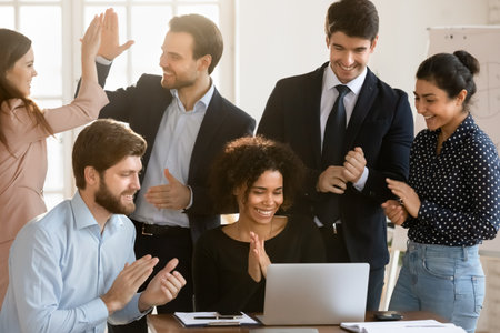 Overjoyed multiracial businesspeople look at laptop screen celebrate shared team business victory...