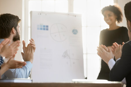 Close up of overjoyed diverse businesspeople clap hands greeting successful female coach or trainer at meeting, excited employees applaud thanking speaker for presentation, acknowledgement conceptの写真素材