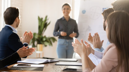Overjoyed multiracial diverse employees applaud meeting greeting female coach or trainer in office, happy excited businesspeople colleagues clap hands thanking speaker for presentation at briefingの写真素材
