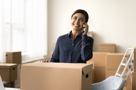Cheerful Indian Internet shop owner girl enjoying work in small commercial storage, packing box with...