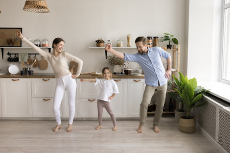 Happy active mom, dad and cute toddler kid dancing in spacious home kitchen, celebrating moving into new apartment with modern interior after buying, rent, renovationの写真素材