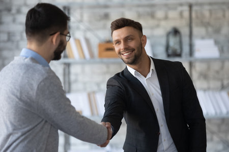 Smiling young businessmen shake hands get acquainted greeting at office meeting, happy motivated male business partners handshake closing dal or making agreement at briefing, partnership conceptの写真素材