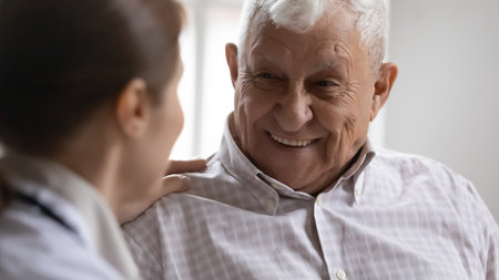 Close up of optimistic old 80s man talk joke with caring female nurse in retirement house, smiling happy mature 70s male patient have pleasant conversation with doctor, elderly healthcare conceptの写真素材