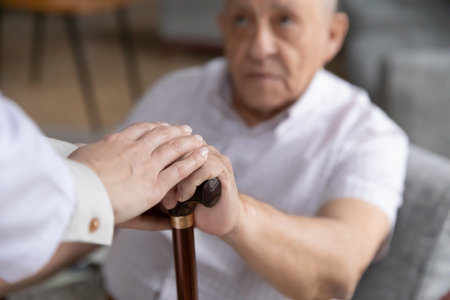Caring nurse hold hands support comfort sick disabled senior 80s male patient with walking stick, caregiver or doctor help stand up ill old man with cane, rehabilitation, elderly healthcare conceptの写真素材