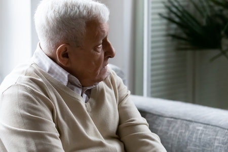 Thoughtful sad elderly 80s man sit on couch in living room look in distance thinking or pondering, feeling lonely in retirement house, pensive upset mature grandfather mourning or yearning at homeの写真素材