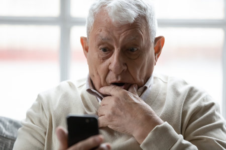 Surprised elderly 80s man using smartphone look at screen shocked by unexpected news or message, stunned mature grandfather amazed by unbelievable text, browsing internet on cellphone gadgetの写真素材