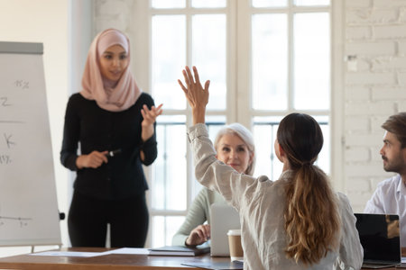 Middle eastern ethnicity woman coach in hijab and seminar participant interaction at group educative meeting in office, employee staff member raise hand ask question, having opinion, solution conceptの写真素材